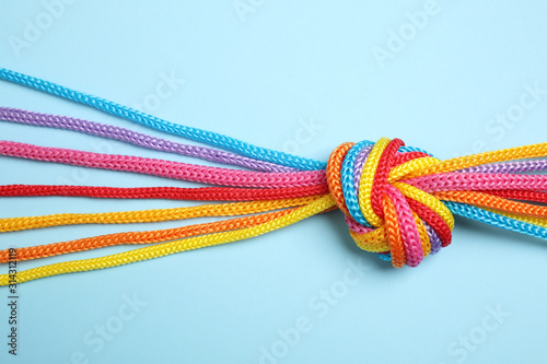 Colorful ropes tied together on light blue background, top view. Unity concept photo