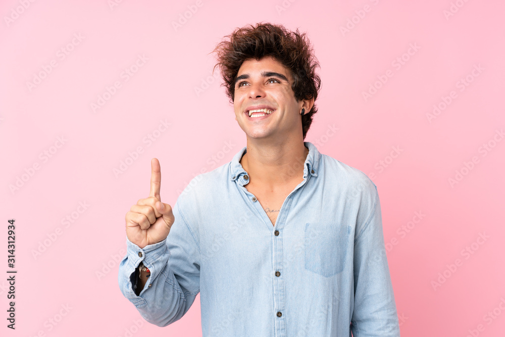 Young caucasian man with jean shirt over isolated pink background pointing up and surprised Young caucasian man with jean shirt over isolated pink background pointing up and surprised