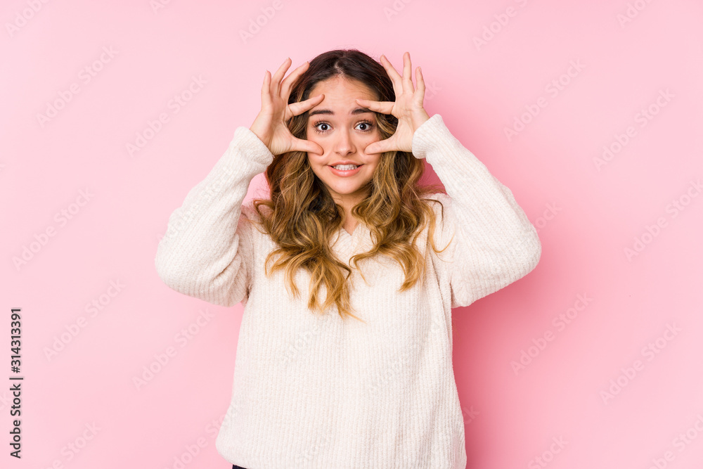 Young curvy woman posing in a pink background isolated keeping eyes opened to find a success opportunity. Young curvy woman posing in a pink background isolated keeping eyes opened to find a success opportunity.