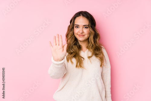 Young curvy woman posing in a pink background isolated smiling cheerful showing number five with fingers.