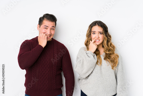 Young couple posing in a white background biting fingernails, nervous and very anxious.