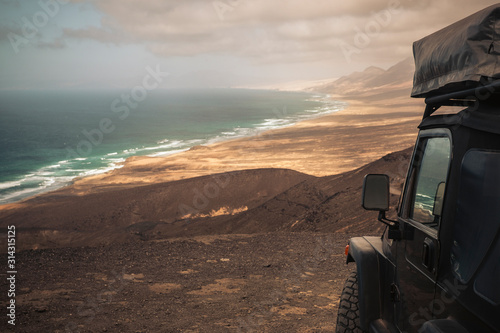 Black off road car with tent on the roof for alternative camping wild vacation concept and wanderlust lifestyle - view of wild beach  and mountains with nobody there © simona