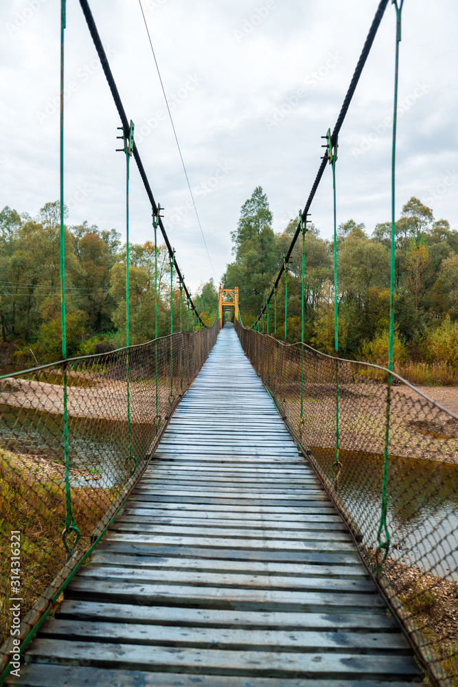 Obraz premium Dramatyczny obraz krajobrazu ciemnego nieba nad lasem i samotnego drewnianego mostu nad rzeką.