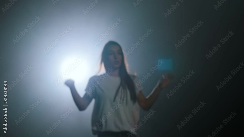 Young woman dancing and walking to the light in dark studio Young woman dancing and walking to the light in dark studio
