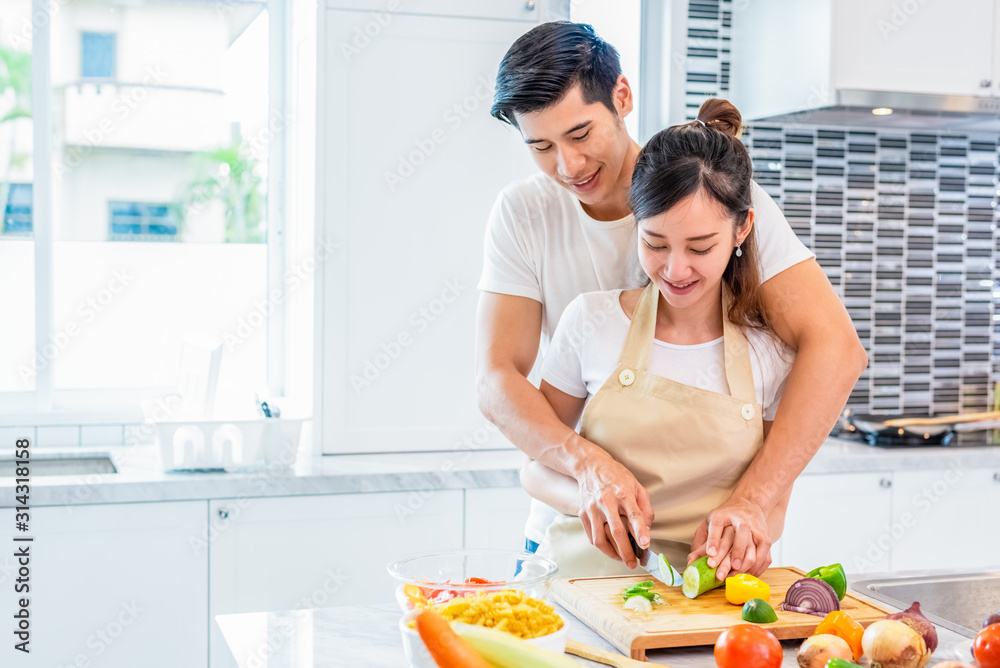 Asian couples cooking and slicing vegetable in kitchen together. Man teaching woman to preparing meal in home. People and lifestyles. Holiday and Honeymoon concept. Valentine day and wedding theme