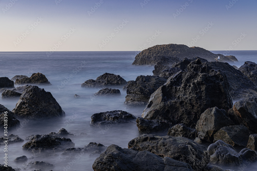Volcanic rocks in Atlantic ocean, long exposure photography, horizon with sunset light, San Juan de la Rambla coastline, Tenerife, Canary islands, Spain
