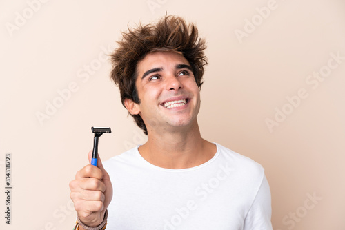 Young handsome man shaving his beard looking up while smiling