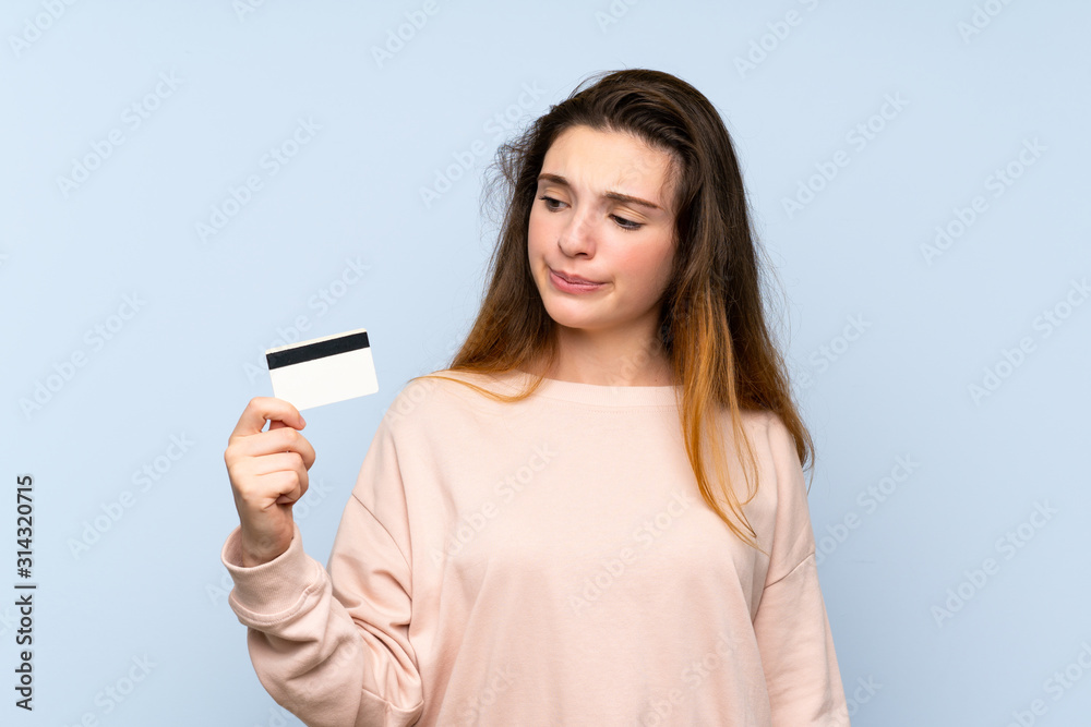 Young brunette girl over isolated blue background holding a credit card