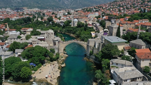 Aerial view of Stari Most old medieval bridge in Mostar, Neretva river, Bosnia and Herzegovina. Tourists walking on the bridge. Summer landscape of old town. Mosque on background.