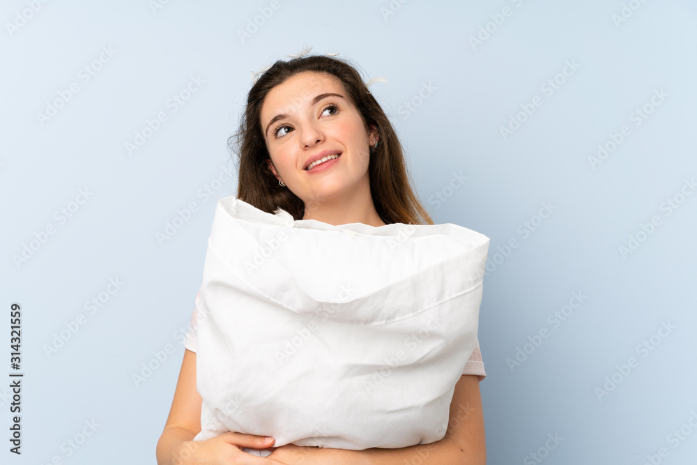 Young woman in pajamas over isolated blue background looking up while smiling Young woman in pajamas over isolated blue background looking up while smiling