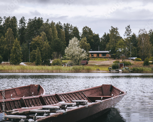 Empty wooden canoe boats on lake shore near building and pine forest in autumn.
