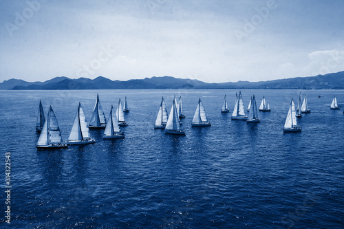 Sailing regatta, group of small water racing boats in Mediterranean, panoramic view with blue mountains on horizon on toning in classic blue color, creative design of 2020