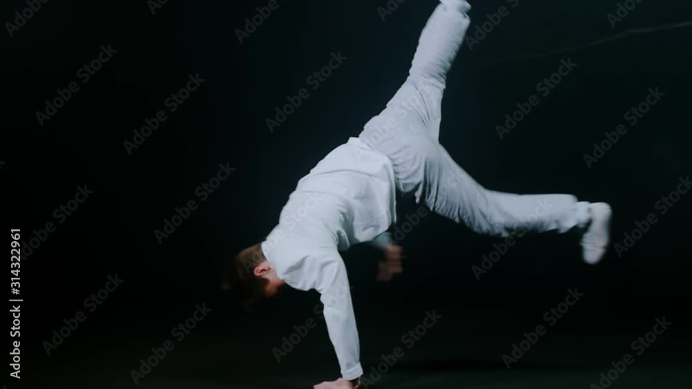 Young man dancer performing break dance trick in the dark studio Young man dancer performing break dance trick in the dark studio
