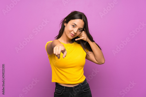 Young brunette girl over isolated background making phone gesture and pointing front