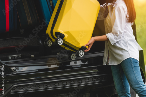 Fotografia Asian woman lifting yellow suitcase into SUV car during travel in long weekend trip