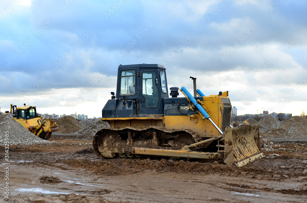 Obraz premium Track-type bulldozer during of large construction jobs at building site. Land clearing, grading, pool excavation, utility trenching, utility trenching and foundation digging. Earth-moving equipment.
