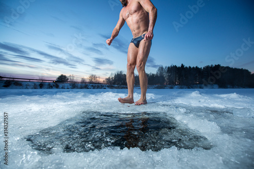 Young man with beard stands barefoot on the ice after swimming in the winter lake