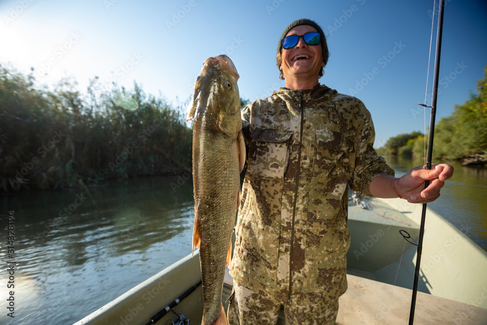 Happy fisherman holds the big Asp fish being on the river in the boat Happy fisherman holds the big Asp fish being on the river in the boat