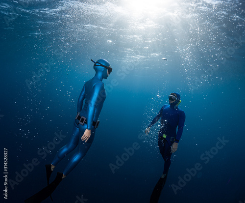 Two freedivers ascend surrounded by bubbles