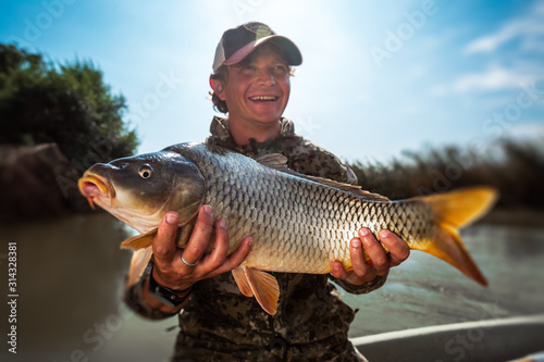 Fototapeta Naklejka Na Ścianę i Meble -  Happy young fisherman holds the big Carp fish (Cyprinus carpio) and smiles