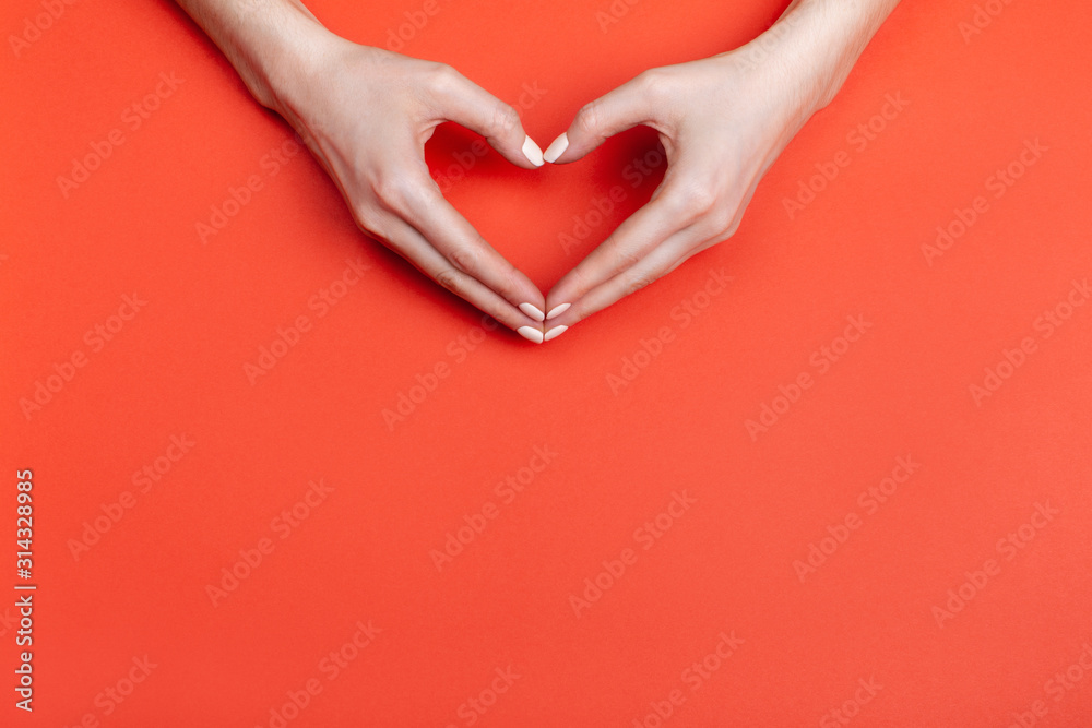 Obraz premium Female hands show a heart symbol on a red background. Place for text.