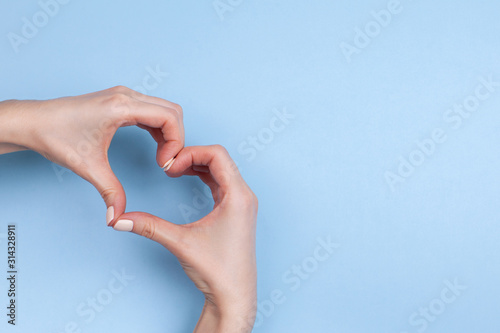 Female hands show a heart symbol on a light blue background. Place for text.