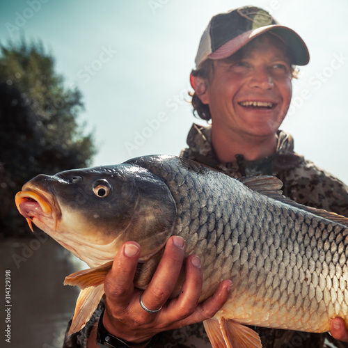 Happy young fisherman holds the big Carp fish (Cyprinus carpio) and smiles
