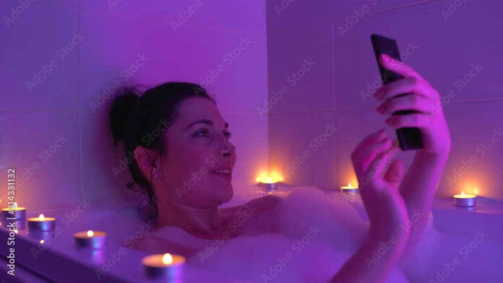 Happy female taking selfie on smartphone in romantic bathroom atmosphere, relax Happy female taking selfie on smartphone in romantic bathroom atmosphere, relax