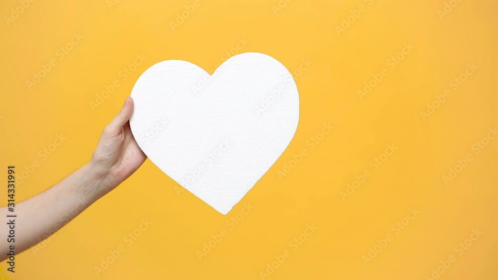Female blogger hold in hand white clear empty blank heart, showing thumb up isolated on yellow orange background. Like blogging blog social network concept. Copy space. Advertising area mock up. Female blogger hold in hand white clear empty blank heart, showing thumb up isolated on yellow orange background. Like blogging blog social network concept. Copy space. Advertising area mock up.