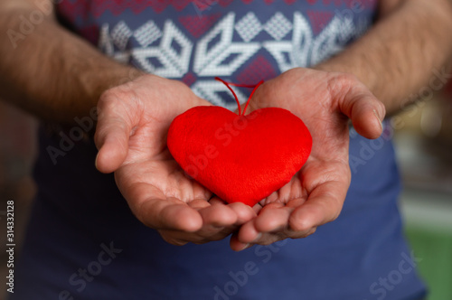 a man holds a bright red plush heart in his palms  holds it out to someone as a sign of love and care