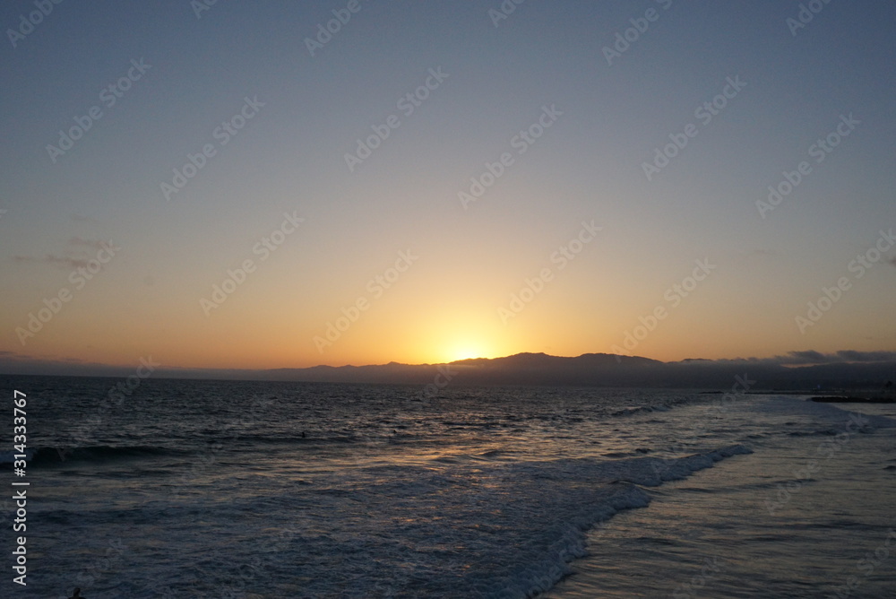 Sunsetting behind the mountains just off the beach of Santa Monica, California with a surfer and paraglider enjoying the views Sunsetting behind the mountains just off the beach of Santa Monica, California with a surfer and paraglider enjoying the views