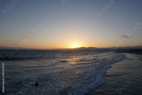 Sunsetting behind the mountains just off the beach of Santa Monica, California with a surfer and paraglider enjoying the views