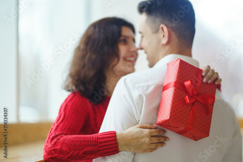Happy couple with gift hugging. Red gift box in the hands of a couple in love. Valentine's Day, holiday and surprise concept. Lovers give each other presents. Relationship and love concept.