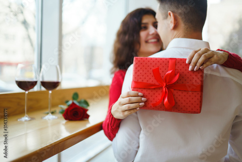 Cheerful couple with gift in hands enjoying each other. Romance at restaurant. Valentine's Day, holiday and surprise concept. Lovers give each other presents. Relationship and love concept.