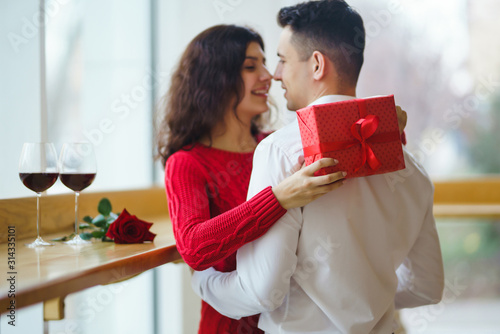 Cheerful couple with gift in hands enjoying each other. Romance at restaurant. Valentine's Day, holiday and surprise concept. Lovers give each other presents. Relationship and love concept.