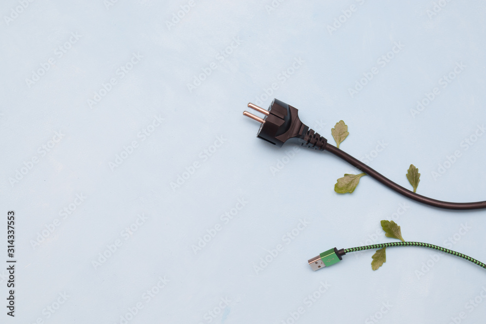 electric plug with green leaves on a blue background, top view okpia place, energy conservation concept electric plug with green leaves on a blue background, top view okpia place, energy conservation concept