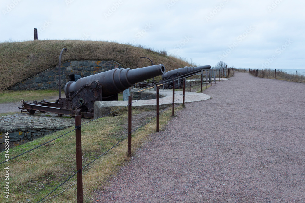 Old cast-iron artillery Russian guns, old granite fortifications of the island-fort Suomenlinna overgrown with grass, Suomenlinna, gloomy autumn day in Finland.
