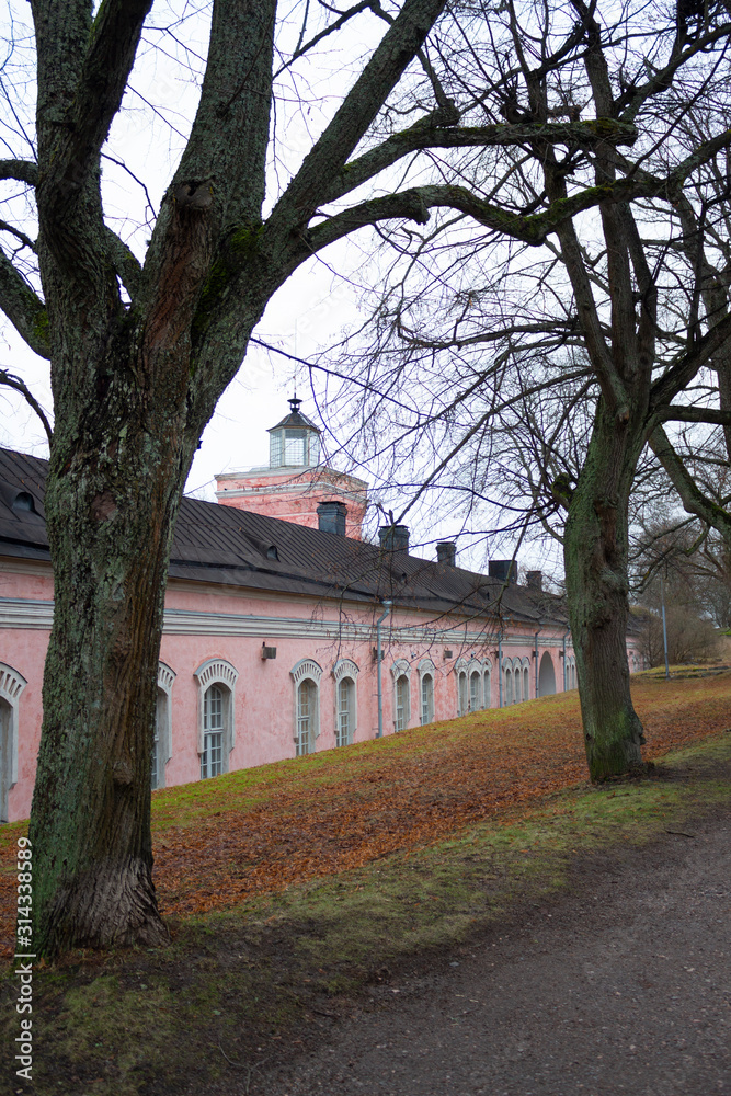 Ancient historical fortification wall with a lighthouse tower above the gate and a park near the wall on the historic island fort Suomenlinna (Sveaborg) in Helsinki in Finland on an autumn day. Ancient historical fortification wall with a lighthouse tower above the gate and a park near the wall on the historic island fort Suomenlinna (Sveaborg) in Helsinki in Finland on an autumn day.