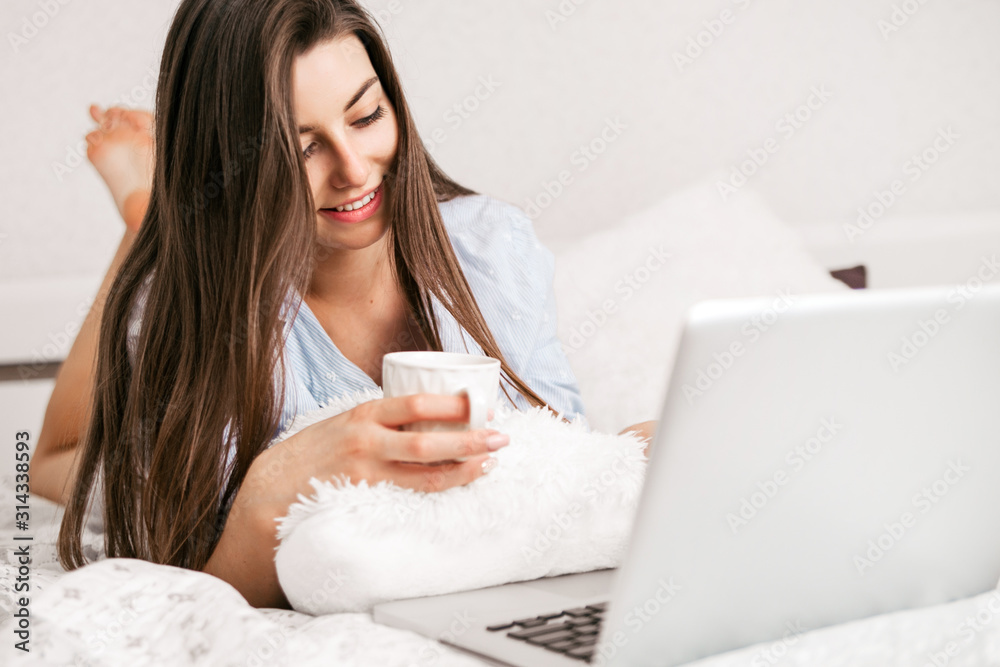 Young smiling woman working on laptop in her bedroom. Happy morning. Young smiling woman working on laptop in her bedroom. Happy morning.