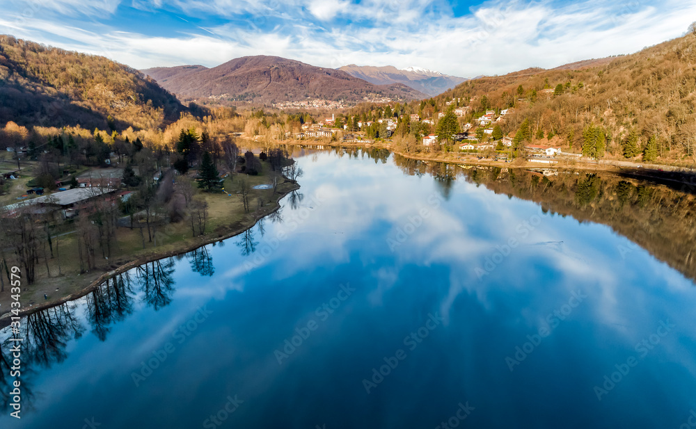 Aerial View of Lake Ghirla with reflections of the clouds and trees in a winter day, Valganna, Italy