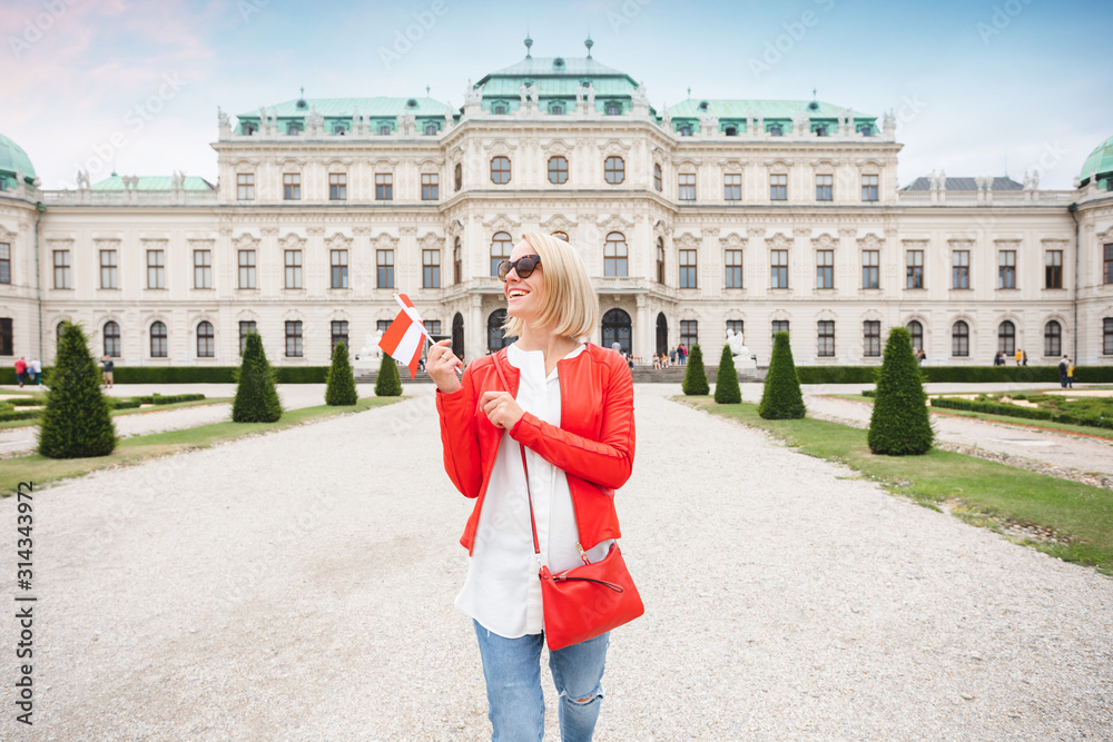 A young female tourist with the Austrian flag enjoys a tour of Vienna in the garden of the Belvedere Palace Complex - obrazy, fototapety, plakaty 