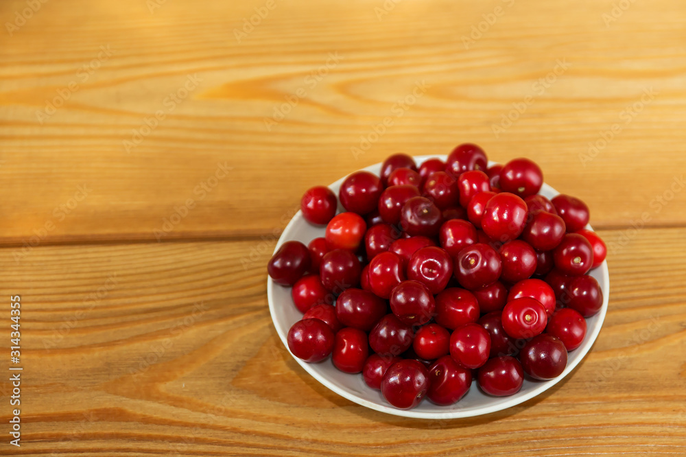 Ripe red cherries on a wooden background. Red berries on a plate on a brown background. Ripe red cherries on a wooden background. Red berries on a plate on a brown background.