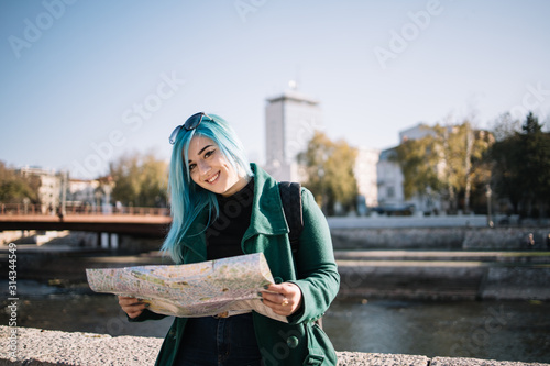 Travel girl leaning on stone fence with map and looking at camera