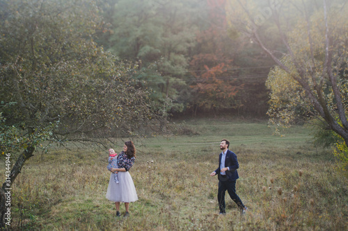 Young happy caucasian couple with little baby girl. Parents and daughter walking and having fun together. Mother and father play with child outdoors. Family, parenthood, childhood, happiness concept.