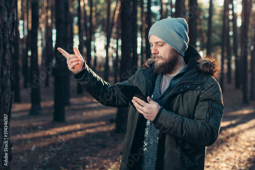 Portrait of adult man walking in the pine forest with digital tablet.