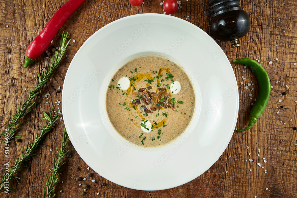 Mushroom cream soup with champignons, garnished with fried mushrooms, olive oil and grated Parmesan cheese in grey bowl on a wooden background. Healthy diet. Top view food