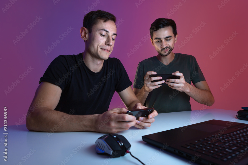 Two gamers taking a break during video game to check smartphones for notifications Two gamers taking a break during video game to check smartphones for notifications