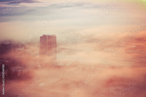 Aerial view of a foggy sunrise over a residential and industrial area of a city. Fog layered over houses below early morning sunrise.