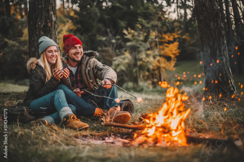 Fotografia Traveler couple camping and roasting marshmallows over the fire in the forest after a hard day