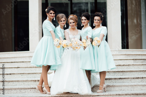 Bridesmaids in turquoise dresses are standing near the bride and groom outdoors. Beautiful girls on wedding day posing on the stairs. Elegant friends with bouquets. Autumn. Wedding.